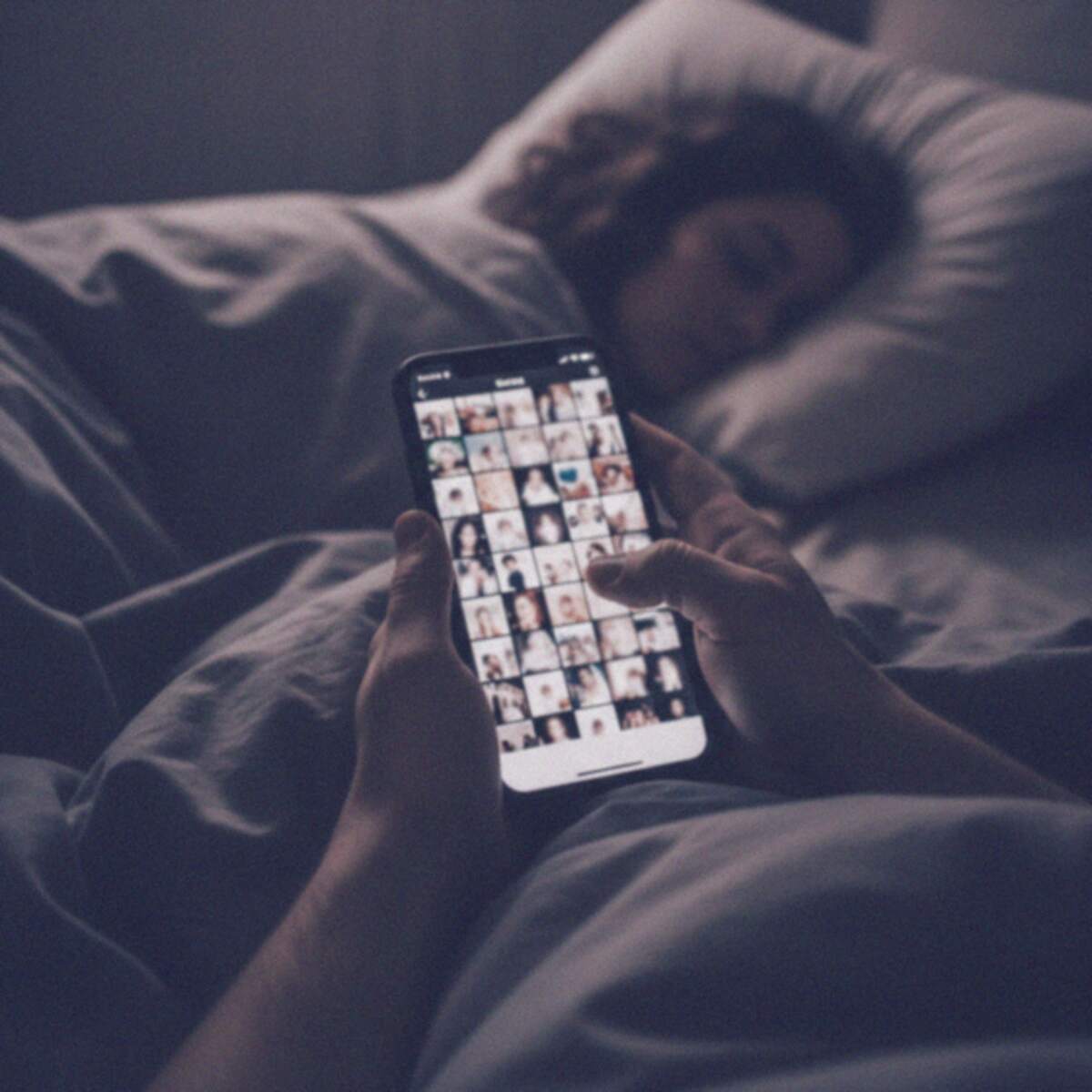 Alguien revisa una cuadrícula de fotos borrosas en un celular, en la cama, mientras la dueña duerme